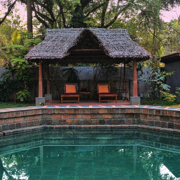 A pool with a thatched-roof gazebo seating area.