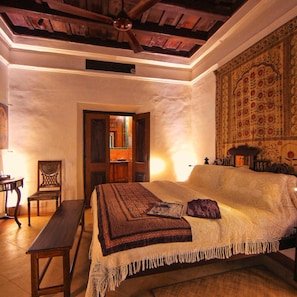 A bedroom with a bed, a bench, a chair, and a tapestry.
