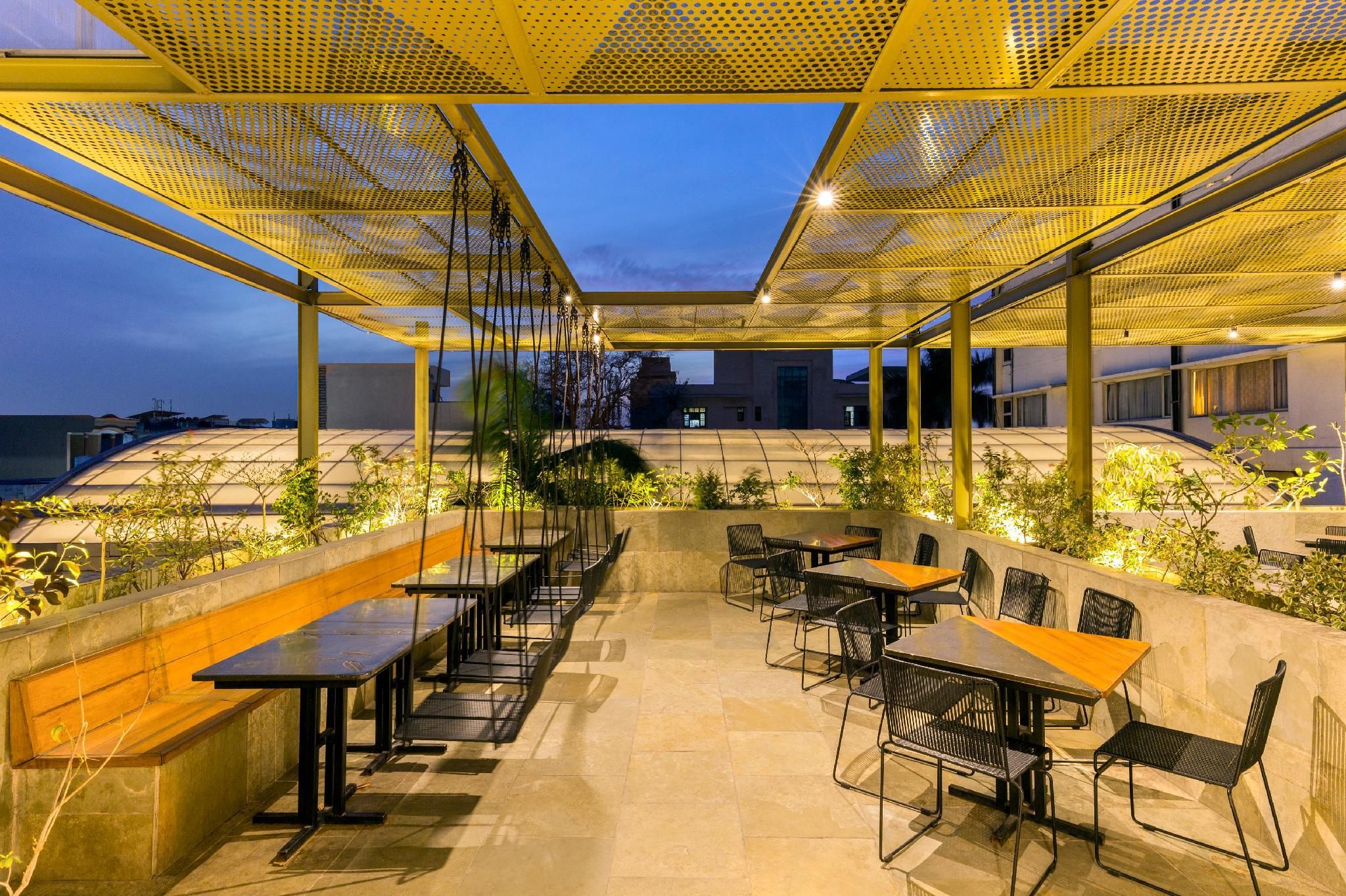 An outdoor dining area with tables and chairs, a pergola structure, and a view of the cityscape.