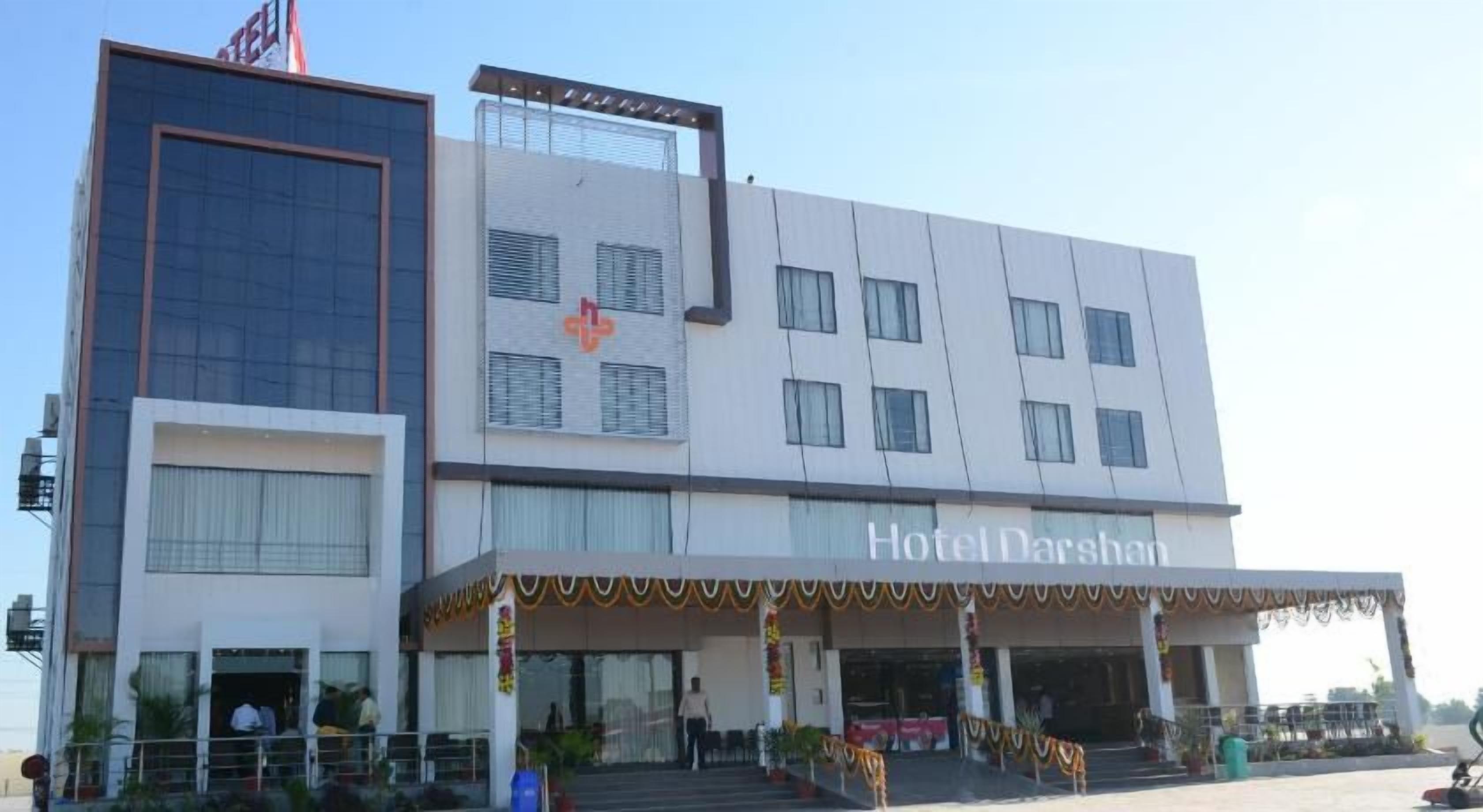 A hotel with a modern facade, a prominent entrance, and a sign indicating it is Hotel Darshan.