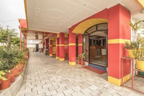 A covered walkway with tiled flooring, red and yellow pillars, and potted plants. - Hotel Jhanvi Dale (Haridwar)