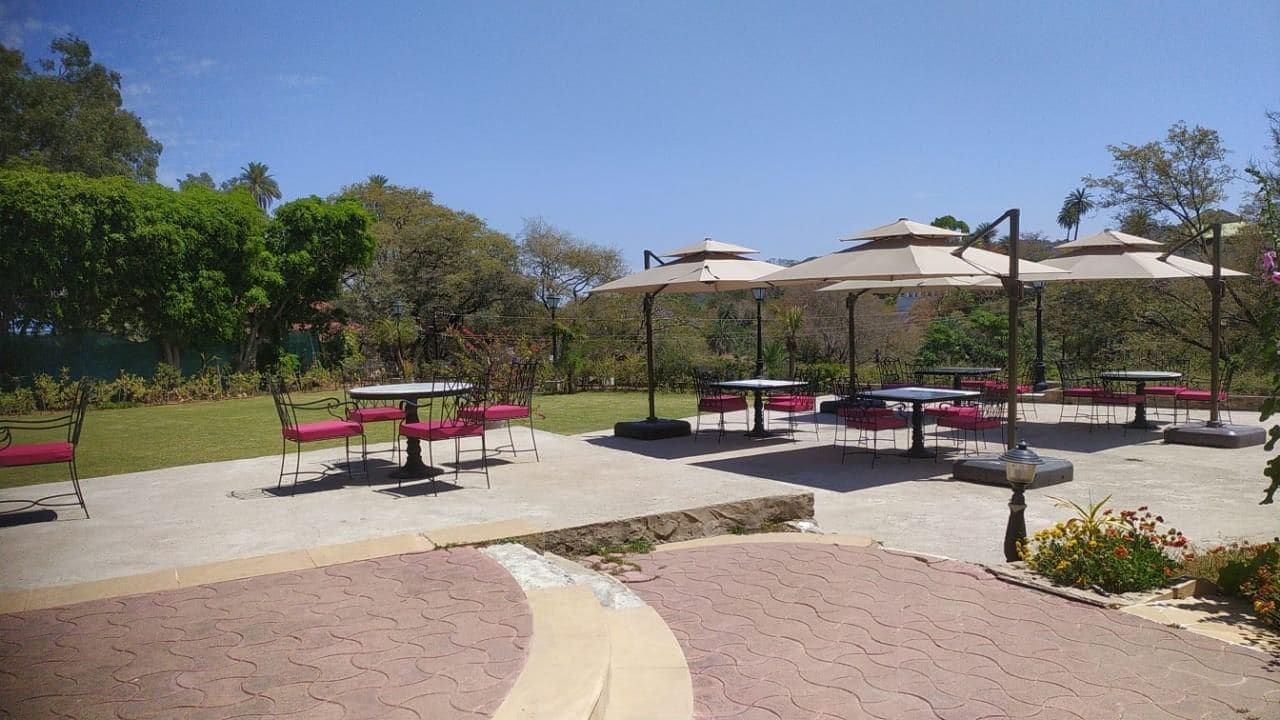 An outdoor patio area with tables and chairs, surrounded by greenery and trees.