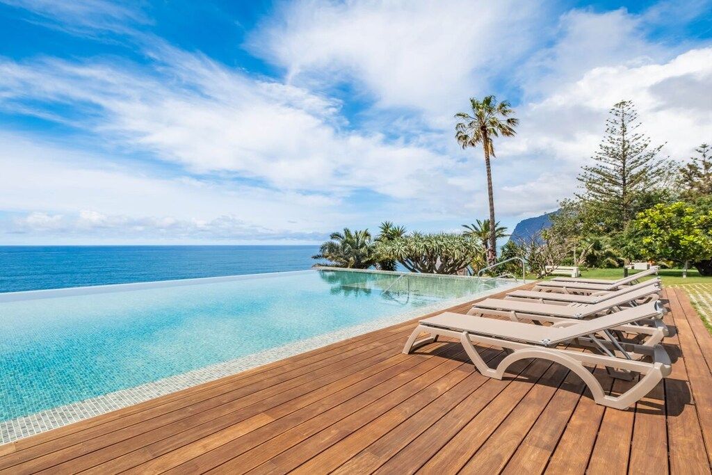 Een houten terras met lounge fauteuils met uitzicht op een heldere blauwe oceaan.