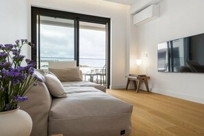 A modern living room with a sofa, a potted plant, a table with a lamp, and a large window with a view. - Holiday apartment with 2 bedrooms (Funchal)