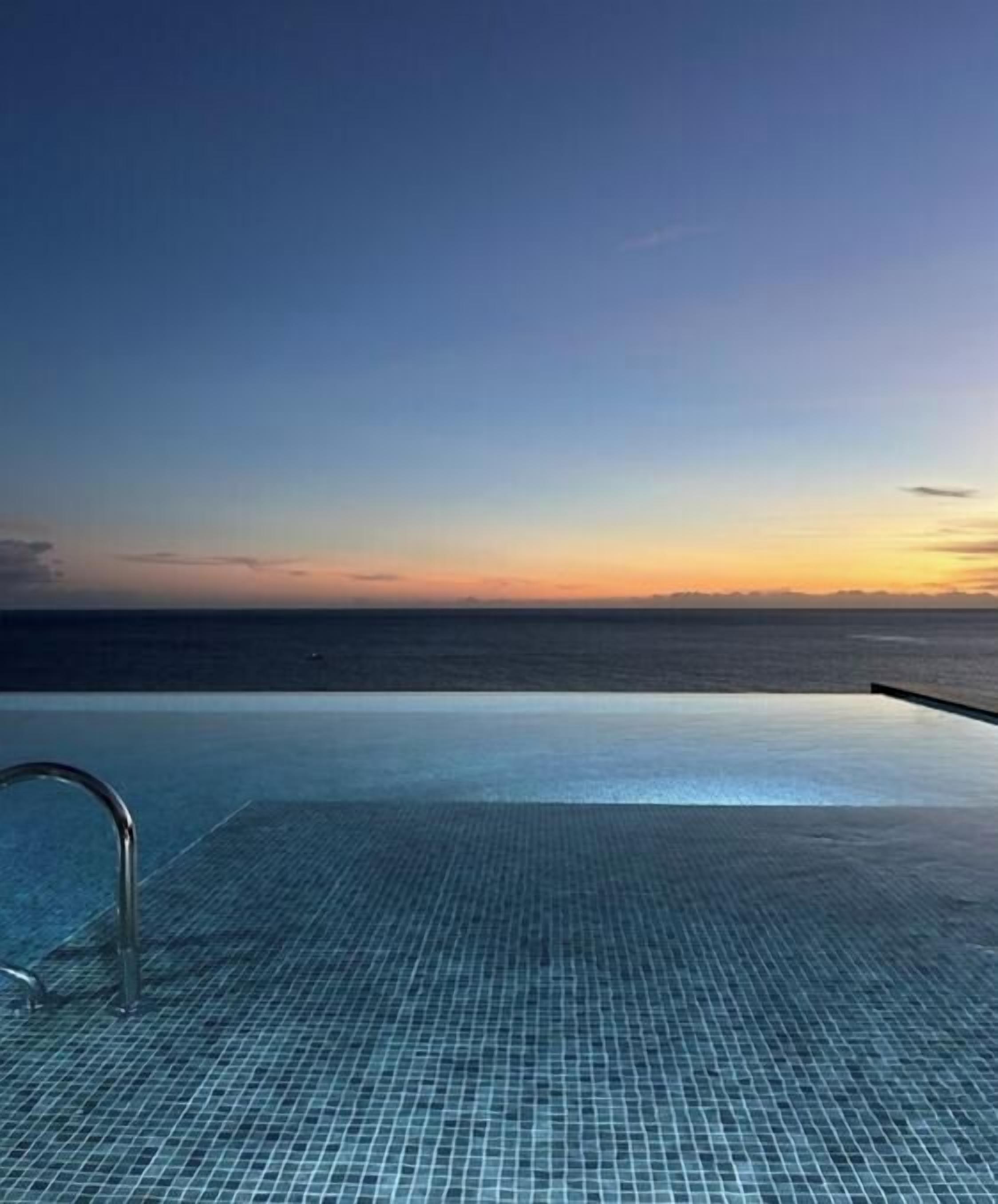 An infinity pool with a view of the ocean at sunset.