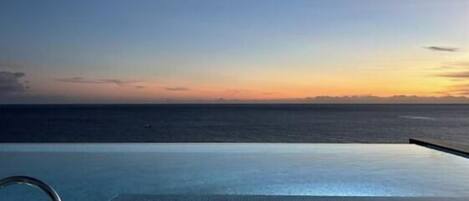 An infinity pool with a view of the ocean at sunset.