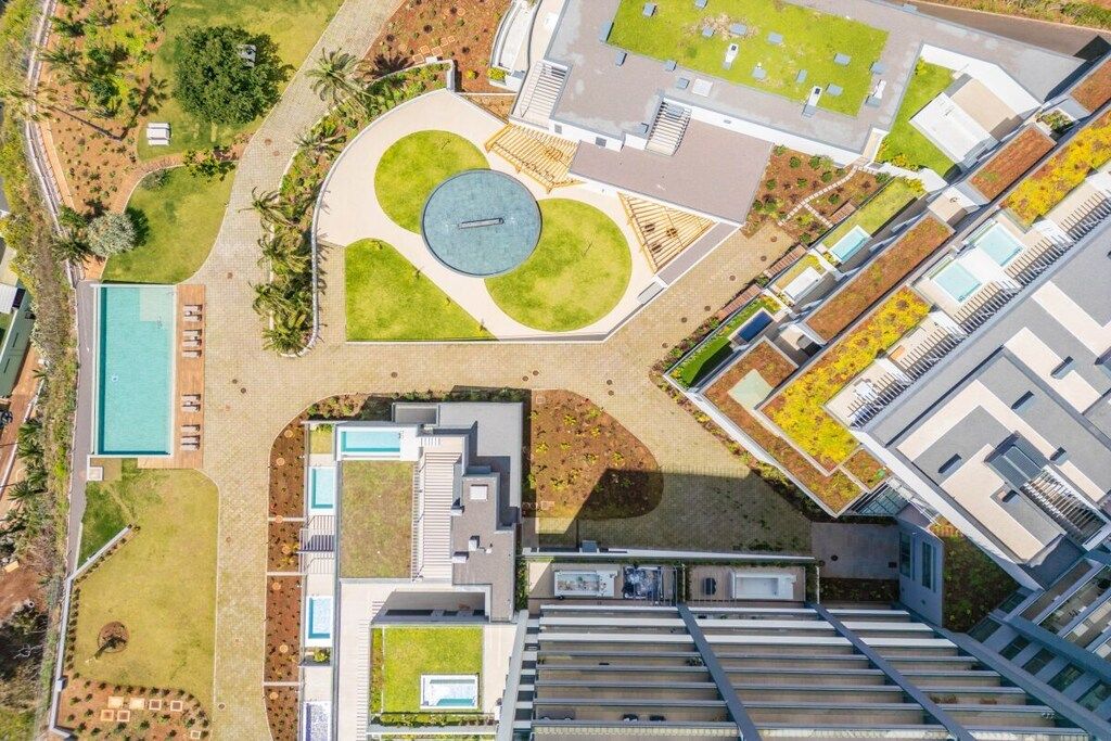 An aerial view of a modern building with a central courtyard, surrounding greenery, and a swimming pool.