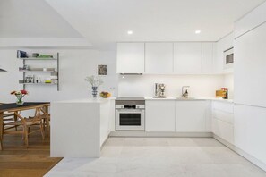Cuina moderna amb armaris blancs, forn integrat i zona de menjador amb taula i cadires de fusta.