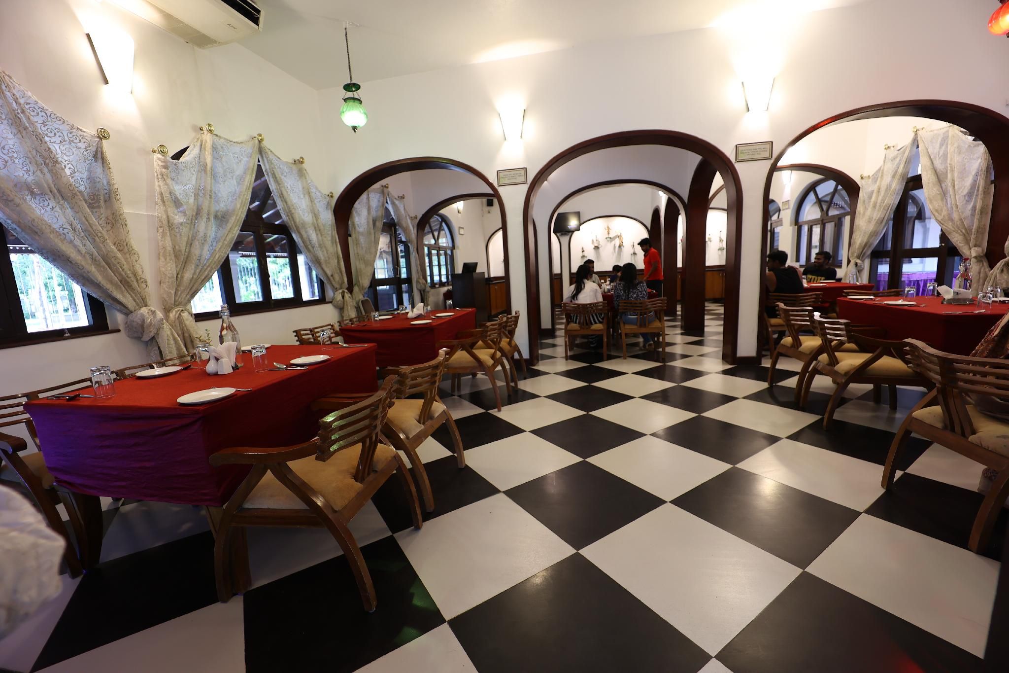 A restaurant with checkered flooring, wooden chairs, and tables with red tablecloths.