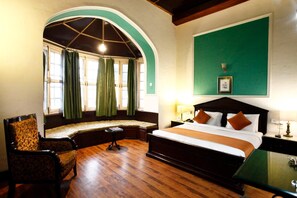 A hotel room with a large bed, a seating area with a bench, a chair, and a desk with a lamp. - Palace Belvedere (Nainital)