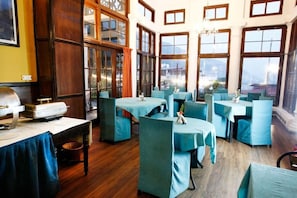 A restaurant with multiple tables and chairs, large windows, and a view of the outside. - Palace Belvedere (Nainital)