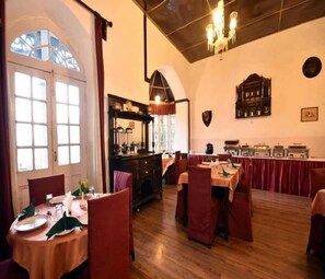 A dining area with multiple tables and chairs, a wooden floor, and a chandelier. - Palace Belvedere (Nainital)