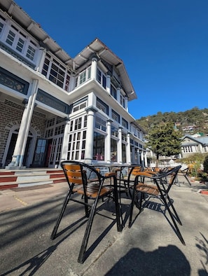 A building with a two-story structure, large windows, and a balcony. There are outdoor tables and chairs in front. - Palace Belvedere (Nainital)
