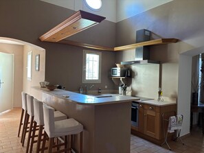 A modern kitchen with a central island, bar stools, a microwave, and a built-in oven. - Holiday Home 'Beautiful Haven Of Peace' with Private Pool, Wi-Fi and Air Conditioning (Mas-Blanc-des-Alpilles)