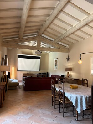 A spacious living area with a high ceiling, a large screen, and a dining table with chairs. - Holiday Home 'Beautiful Haven Of Peace' with Private Pool, Wi-Fi and Air Conditioning (Mas-Blanc-des-Alpilles)