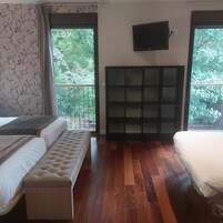 Un dormitorio con cama, una banca, un televisor y una ventana con vista a árboles.