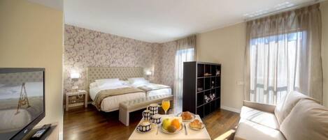 Una habitación de hotel con cama, mesita de noche, televisor, zona de comedor con mesa y sillas, y estantería.
