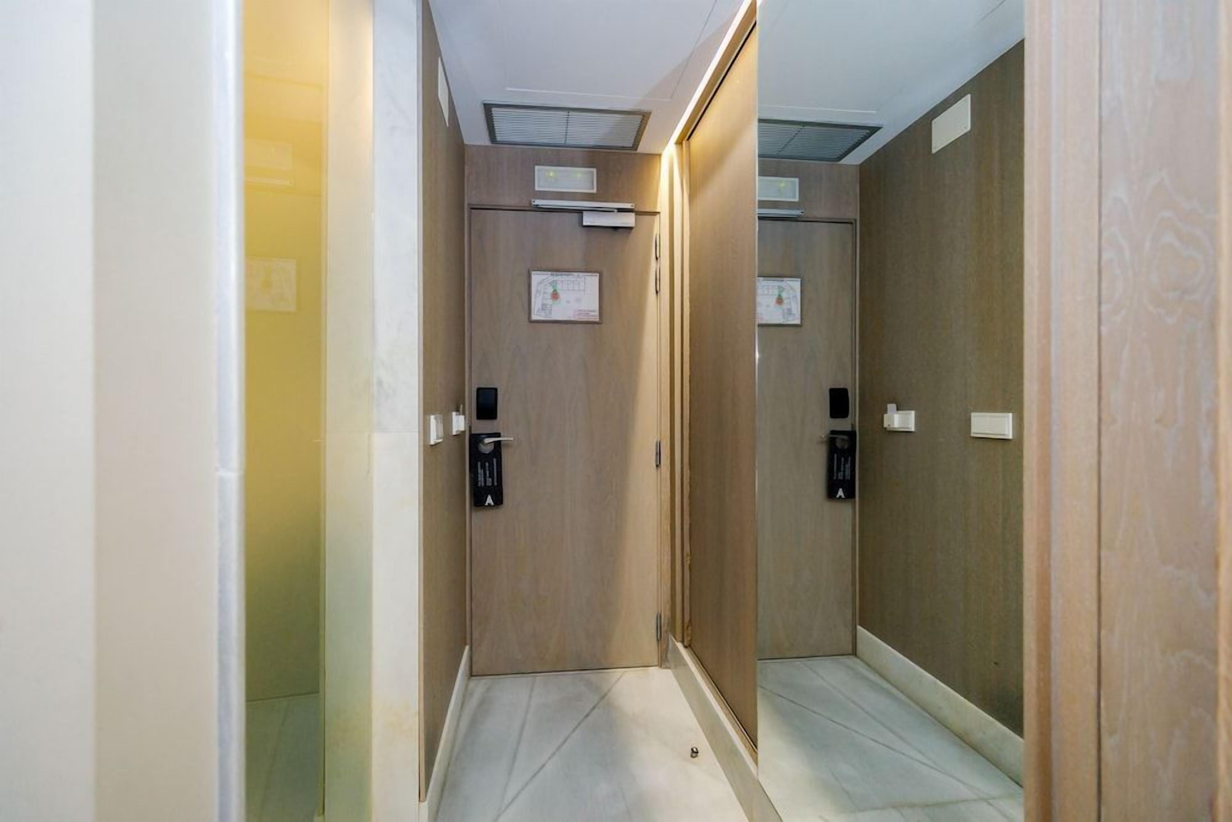 Un pasillo estrecho con puertas de madera, suelo de baldosas e iluminación empotrada en el techo.