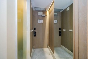 Un pasillo estrecho con puertas de madera, suelo de baldosas e iluminación empotrada en el techo.