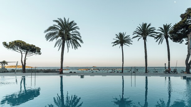 A clear blue pool with palm trees and a beach view. - Sirenis Hotel Goleta And Spa (Ibiza Town)