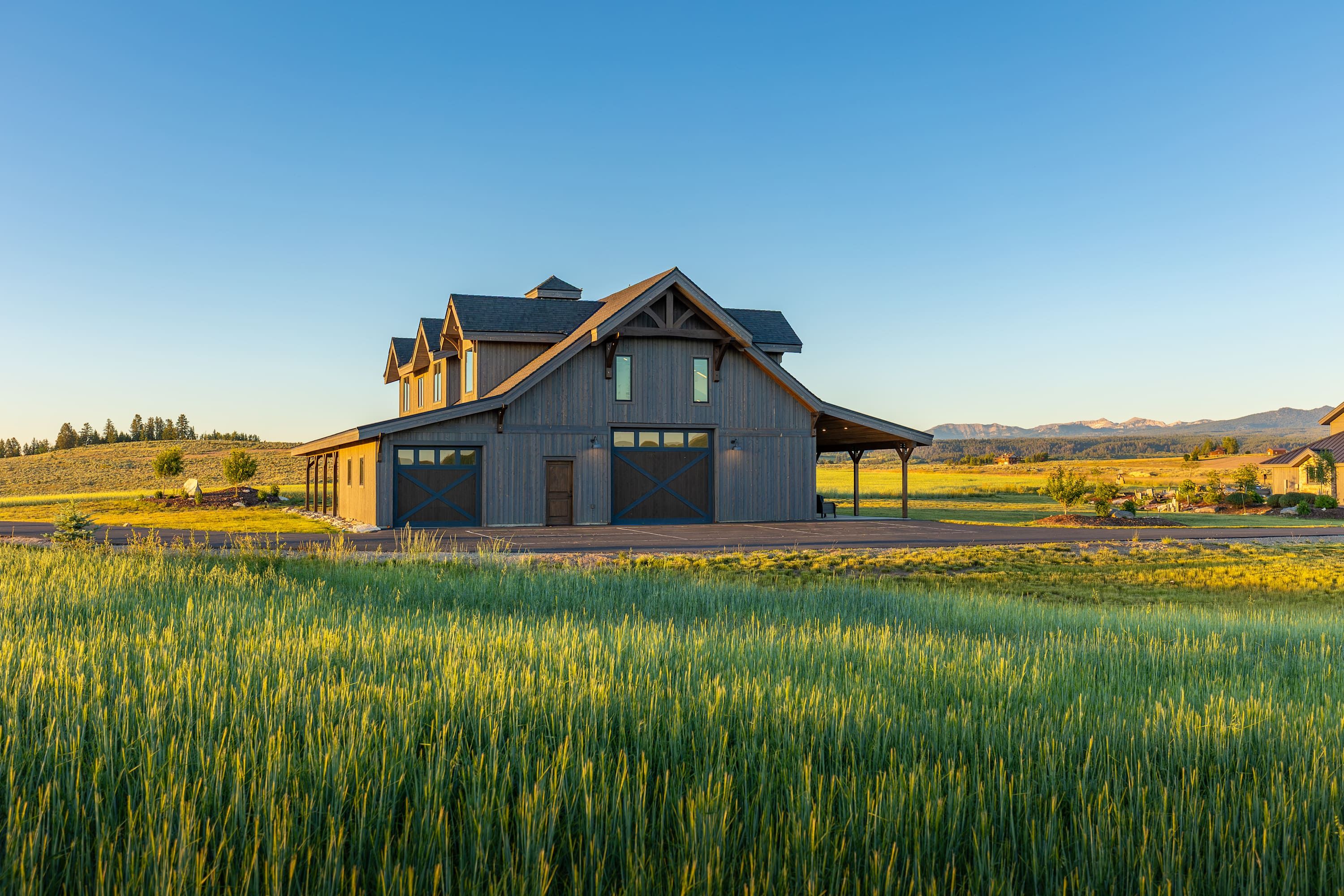 A large wooden barn with a gabled roof and multiple doors, situated in a field with a clear sky.