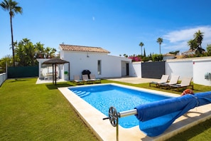A swimming pool with a cover, a patio area with lounge chairs, and a white building with a tiled roof. - « BOHO MAR » - Your next holiday beach villa in Estepona (Saladillo Benamara)