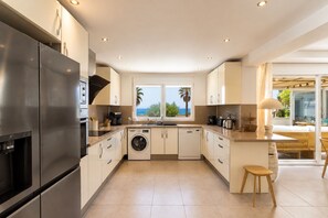 Una cocina moderna con lavadora integrada, un refrigerador grande y vistas al mar a través de las ventanas.