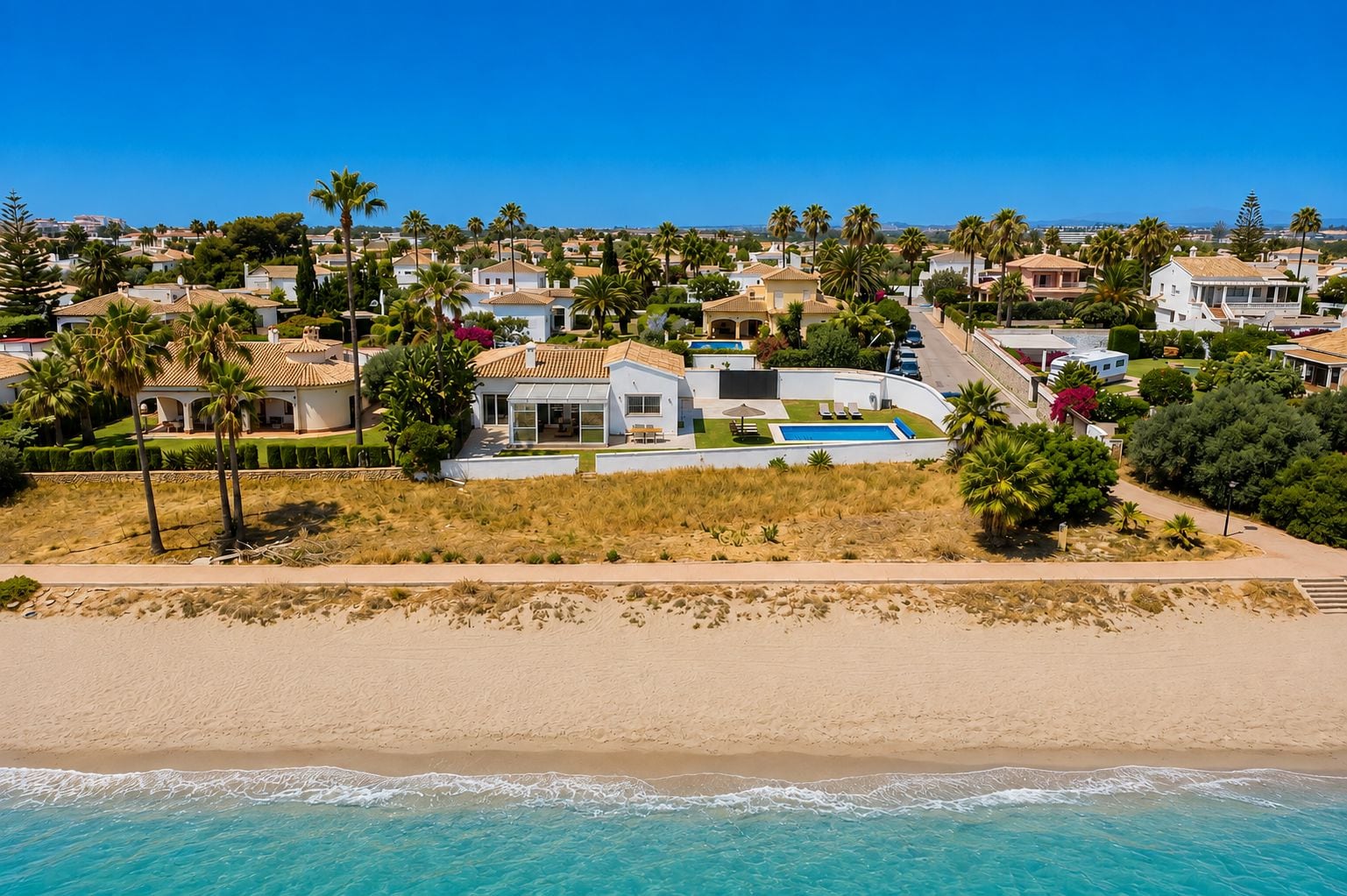 A coastal residential area with houses, a beach, and a clear blue sky.