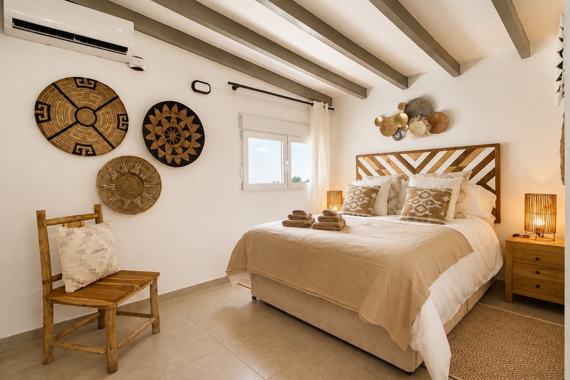 A bedroom with a bed, a wooden chair, a bedside table, a lamp, and decorative wall hangings.