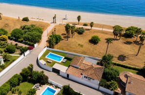 An aerial view of a property with a swimming pool, a beach, and palm trees.