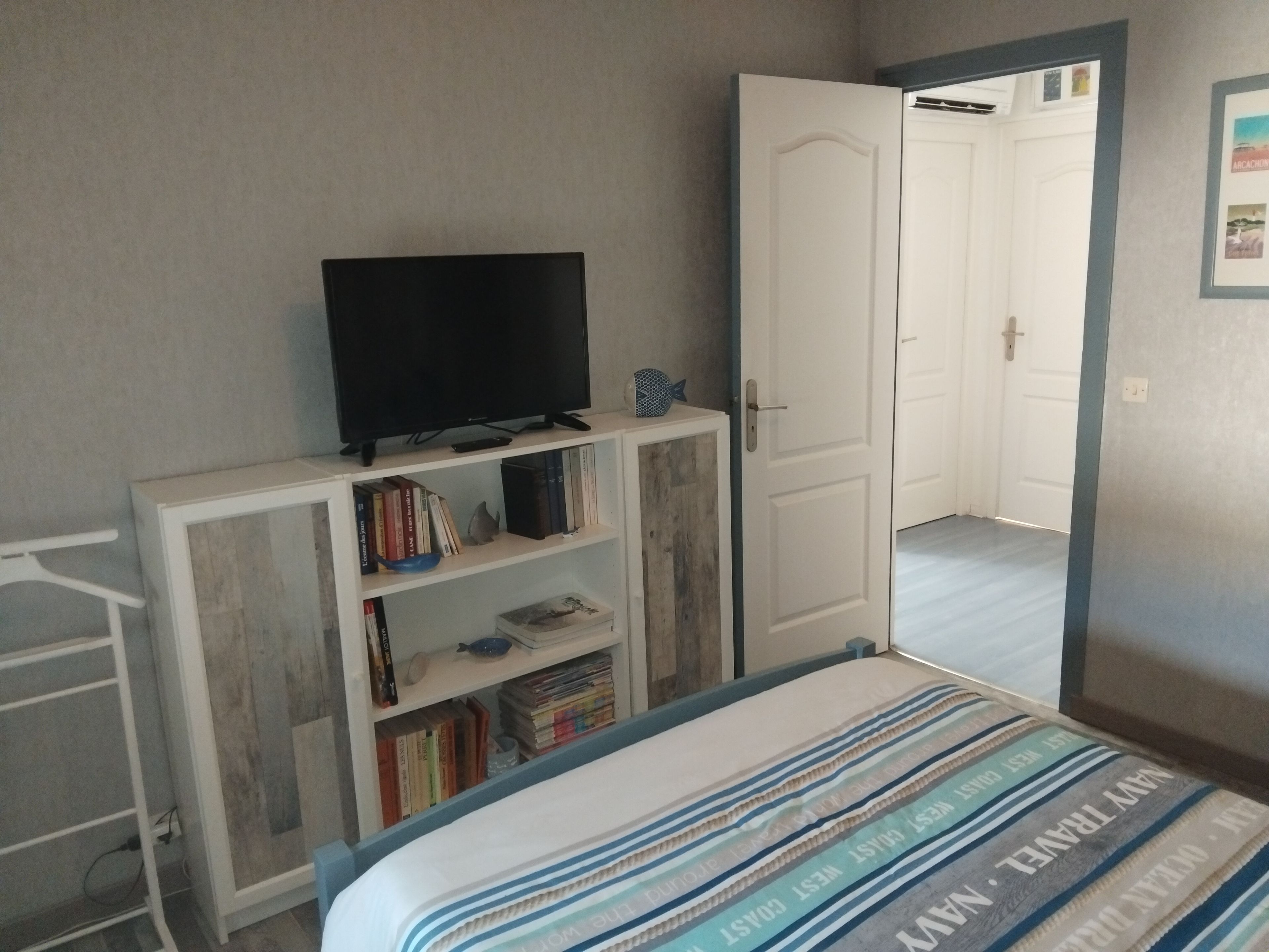 A bedroom with a bed, a television on a stand, a wardrobe, and a door leading to another room.