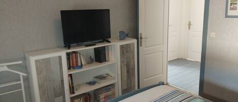 Un dormitorio con una cama, un televisor sobre un mueble, un armario y una puerta que da a otra habitación.