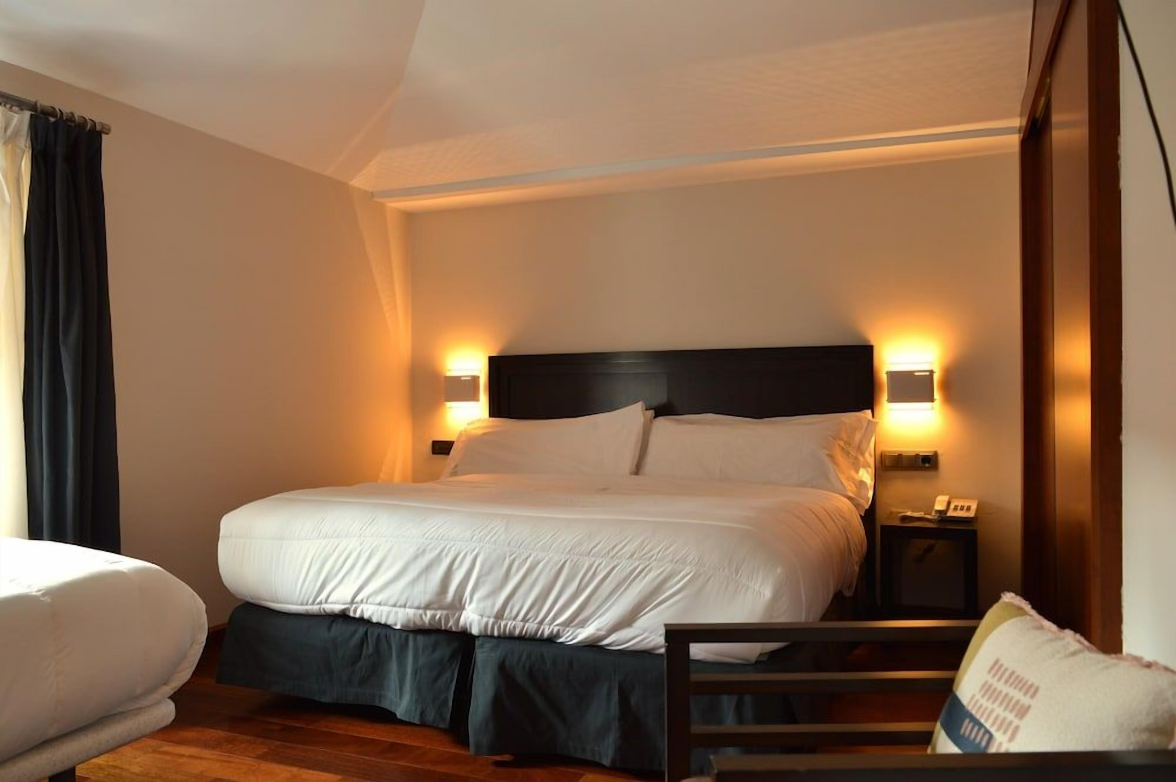Una habitación de hotel con una cama grande, lámparas de noche, una mesita de noche y una silla.