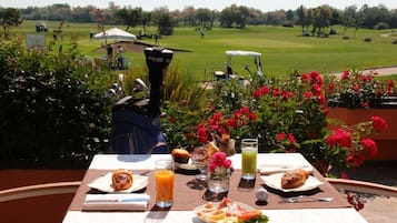 Et bord dækket til morgenmad med udsigt til en golfbane, inklusive en golfvogn og spillere i det fjerne.