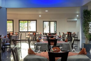 A restaurant with tables set for dining, chairs, and a large potted plant.