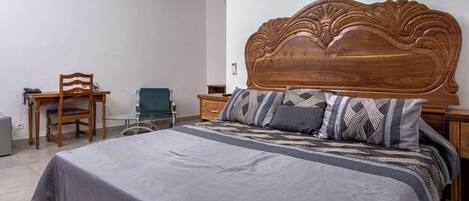 Un dormitorio con una cama grande, cabecera de madera, un escritorio con silla y una mesita de noche.