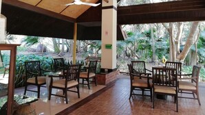 An outdoor seating area with wooden tables and chairs, a ceiling fan, and a view of trees and plants. - Wanathara Health Resort & Spa (Wang Thong)