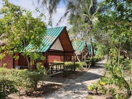 A pathway leading to a row of cabins with green roofs, surrounded by dense greenery and trees.