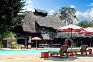 A pool area with lounge chairs and umbrellas, a building with a sloped roof, and a clear sky.