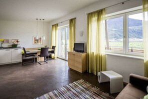 A modern living room with a sofa, a television, a desk with a chair, and a kitchen area. - "Green" on the Sandwiesen farm (Gargazon)