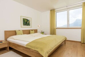 A bedroom with a bed, a nightstand, a bedside table, a window with curtains, and a wall-mounted picture. - "Green" on the Sandwiesen farm (Gargazon)