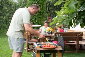 An outdoor dining area with a grill, wooden benches, and a table with a plate of food. - "Green" on the Sandwiesen farm (Gargazon)