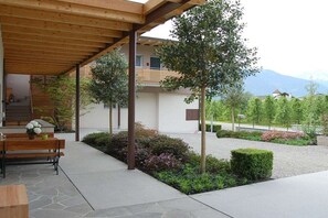 A covered outdoor area with a wooden bench, a table with a vase, and a staircase leading to a building. - "Green" on the Sandwiesen farm (Gargazon)