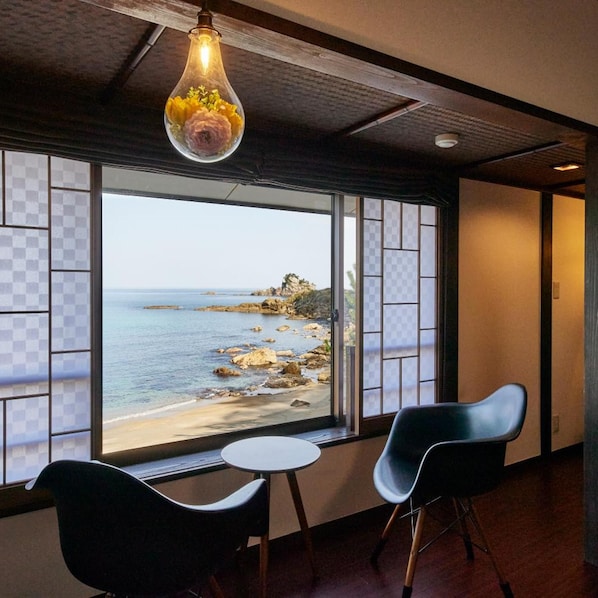 A room with a view of a beach, a round table, two chairs, and a hanging light fixture. - Uminone (Toyooka)