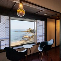 Quarto com vista para uma praia, mesa redonda, duas cadeiras e um lustre.