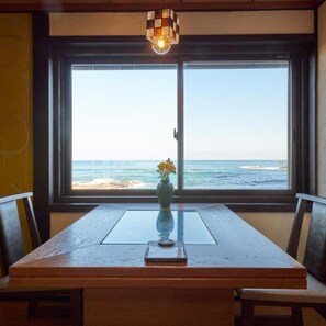 Et spisebord med en vase blomster, et lys og udsigt til havet gennem et stort vindue.