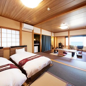 A hotel room with two beds, a desk, a chair, and a view of the sea. - Uminone (Toyooka)