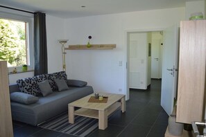 A modern living room with a grey sofa, a wooden coffee table, and a floor lamp. - Holiday apartment in Ladbergen with barbecue (Ladbergen)