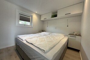 Ein Schlafzimmer mit einem Bett, einem Fenster, einem Nachttisch und einem eingebauten Regal über dem Bett.