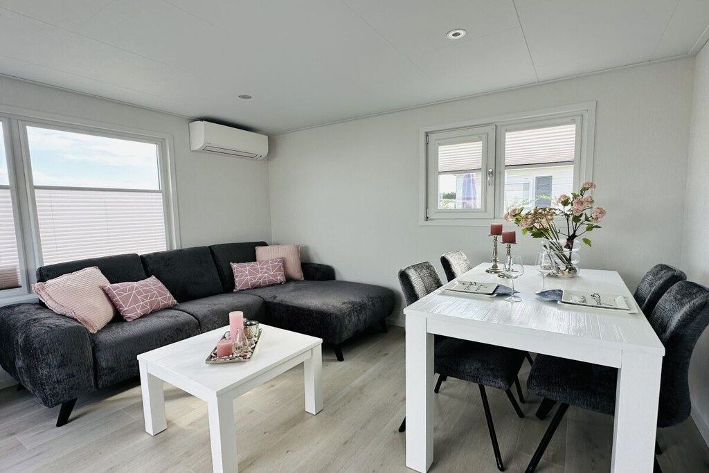 Een moderne woonkamer met een grijze hoekbank, een witte salontafel en een eettafel met stoelen.
